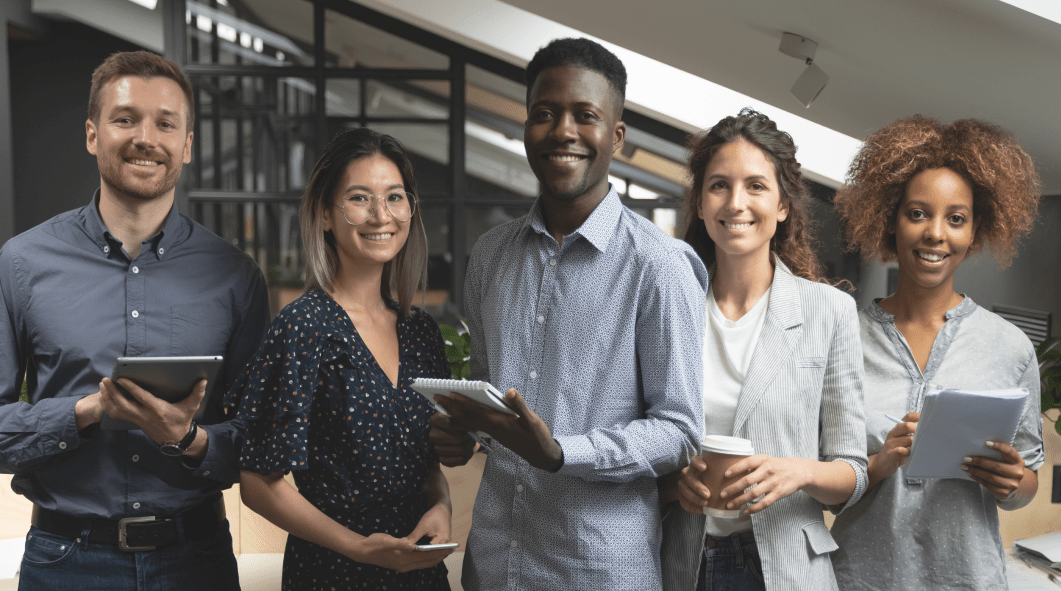stock-photo-portrait-of-happy-successful-multiracial-business-team-standing-with-digital-tablets-notebooks-1563597547 1