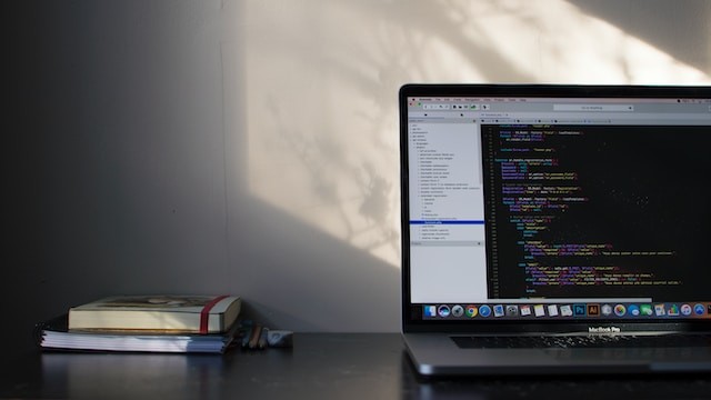 Table with the open laptop displaying code and two books nearby.